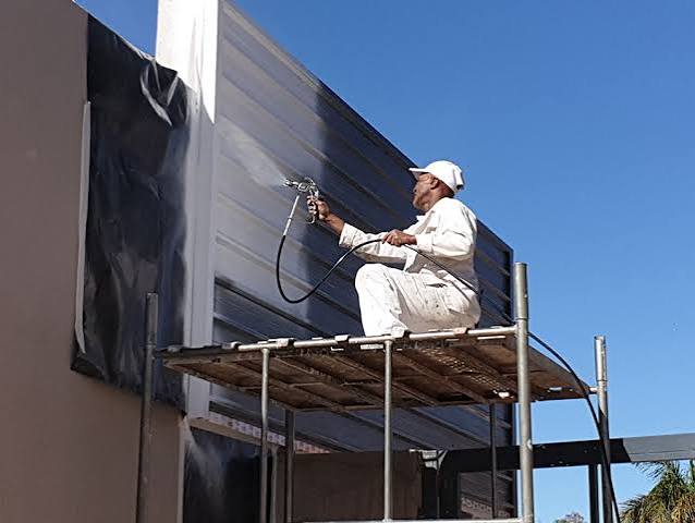 Painter spray-painting an exterior wall